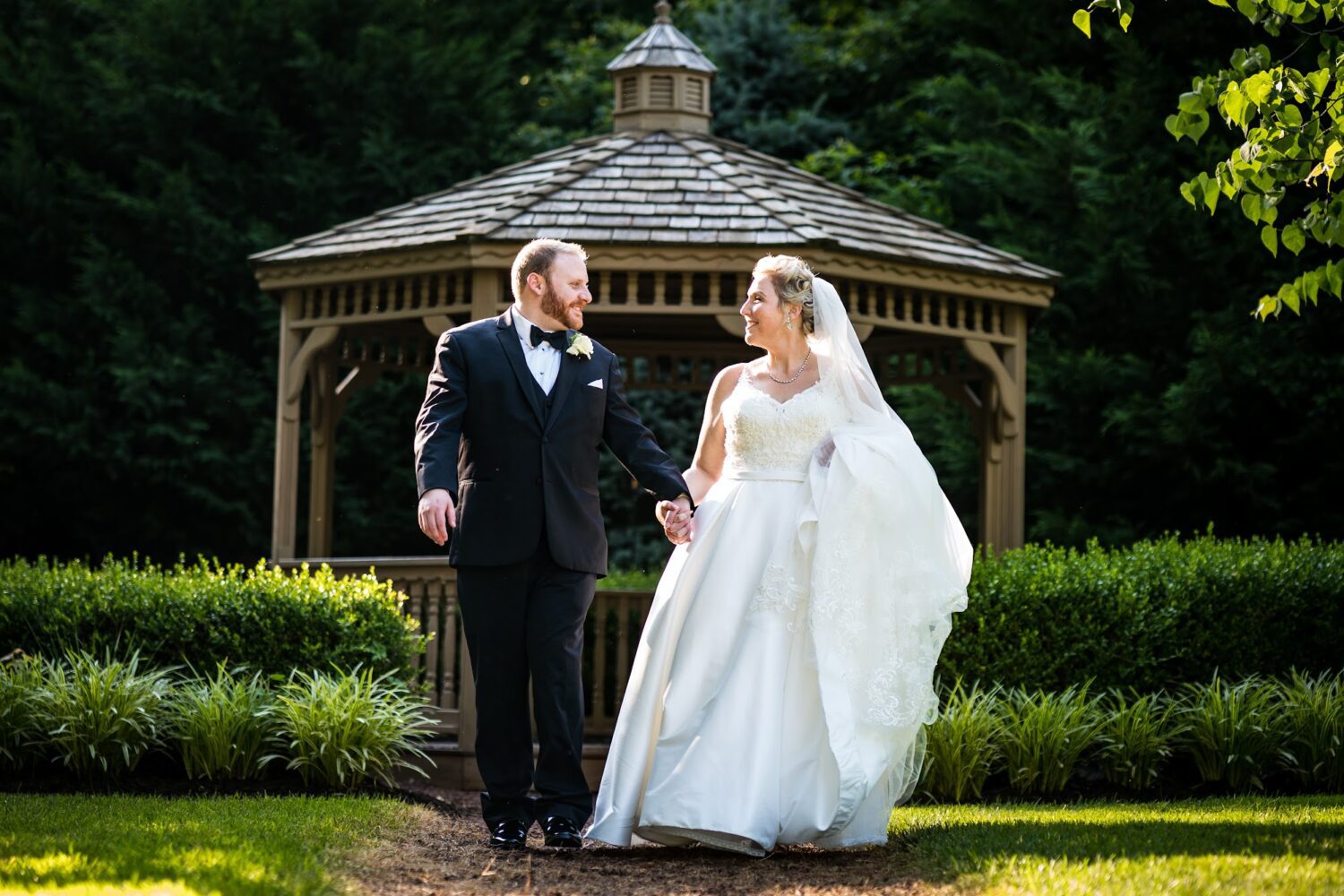Newly wed couple standing infront of gazebo surrounded by green landscaping