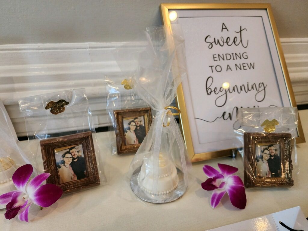 Close up image of bridal shower favors. Cookies realistically painted as a picture frame of the marrying couple. Sign reading "A sweet ending to a new beginning, enjoy!"