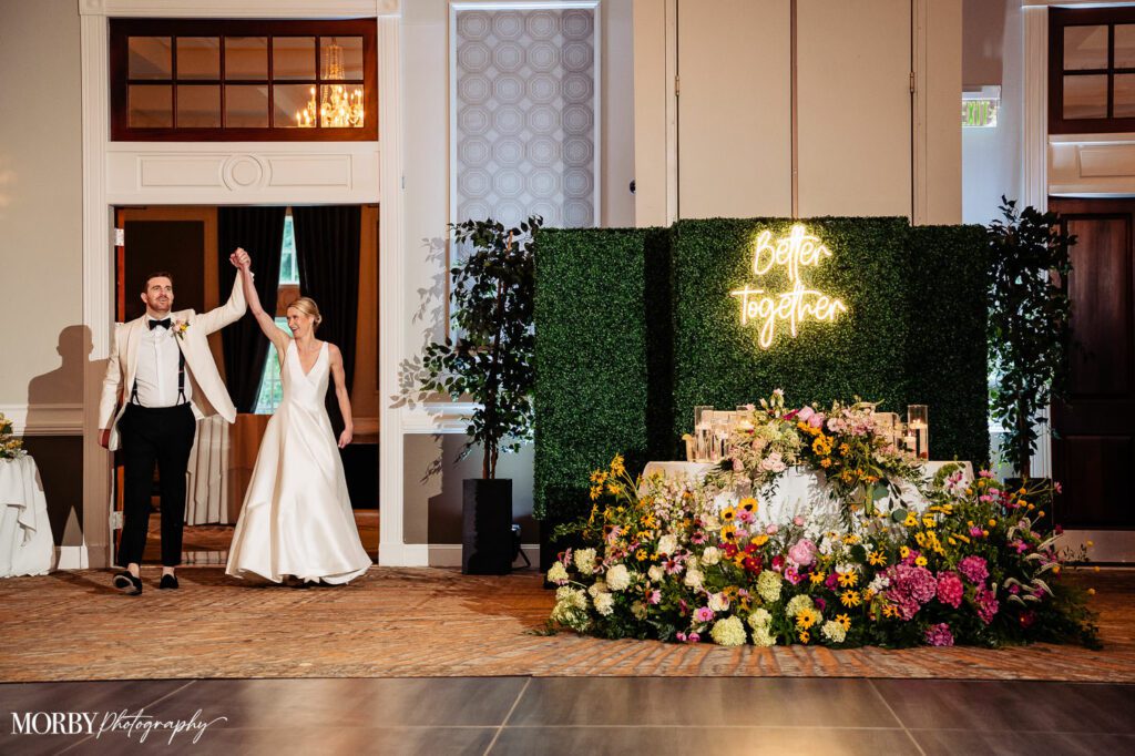 Bride and groom entering the ballroom hand in hand next to floral display.